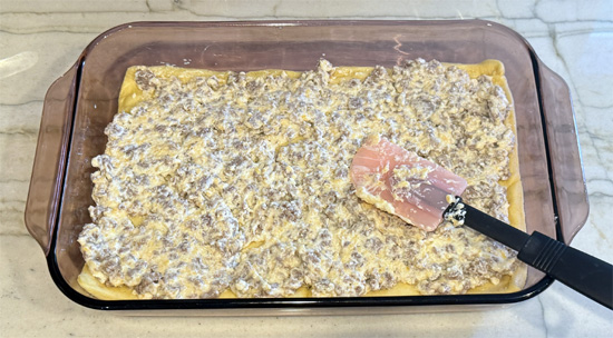Layer the casserole: spread cheese-sausage mixture over the baked crust, add vegetables as the next layer, then top with scrambled eggs.