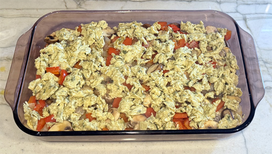 Layer the casserole: spread cheese-sausage mixture over the baked crust, add vegetables as the next layer, then top with scrambled eggs.