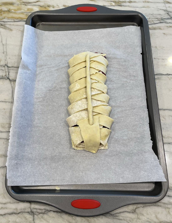 Take the last two strips off. Use one to cover the front, roll the second into a long string, and lay across the top of the pastry.