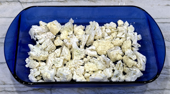 Cover the bottom of the prepared baking dish with the chopped cauliflower. Sprinkle 1/4 teaspoon of salt and 1/4 teaspoon of black pepper over the cauliflower.