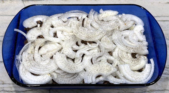 Add the sliced onions on top of the ground beef. Sprinkle 1/4 teaspoon of salt and 1/4 teaspoon of black pepper over the sliced onions.