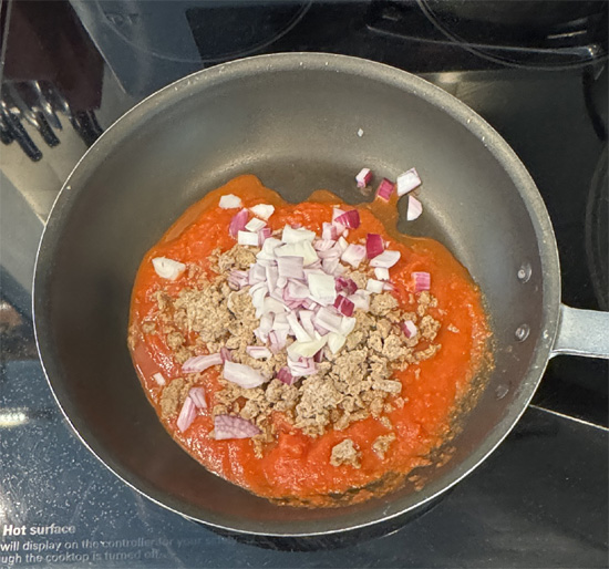 Put the pasta sauce, frozen beef crumbles and chopped onion in a pan over medium heat. Stir and cook for five minutes, until it's heated up. 