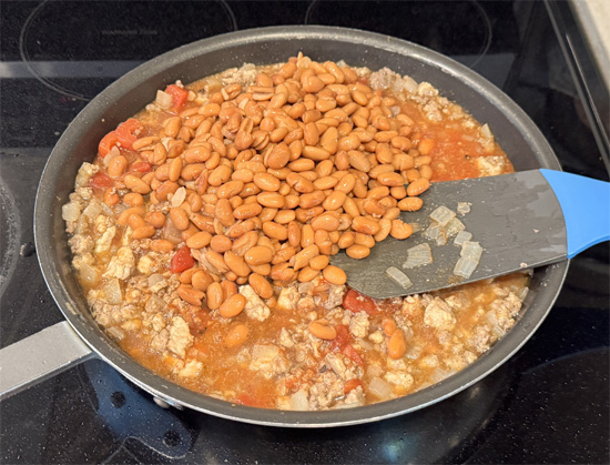 Add the fire-roasted tomatoes, tomato sauce, pinto beans, salt, and black pepper to the pan. Stir it all together. Let the mixture simmer for about 5-6 minutes, allowing the flavors to combine.