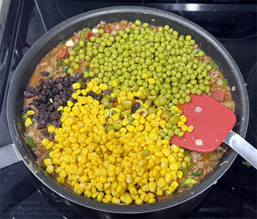 Once the beef is boiling, stir in the peas, corn, raisins, olives and potatoes. 