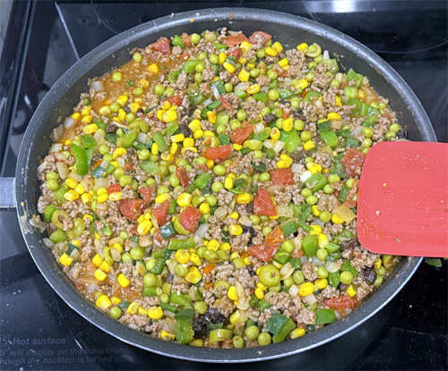 Once the beef is boiling, stir in the peas, corn, raisins, olives and potatoes. 