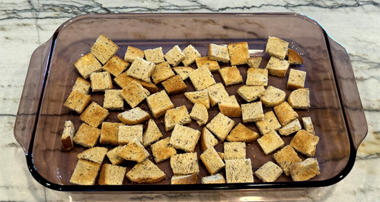 Toast the bread then cut it into cubes. Spread HALF the cubes on the bottom of a 9x13 inch casserole dish. 