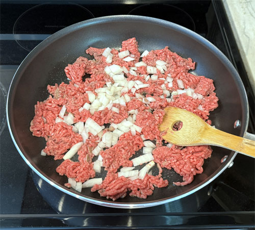 Heat a large skillet over medium heat. Once it's hot, lightly coat it with olive oil spray. Then, add the beef and chopped onion. Break apart and turn the meat and onions until it's no longer pink.