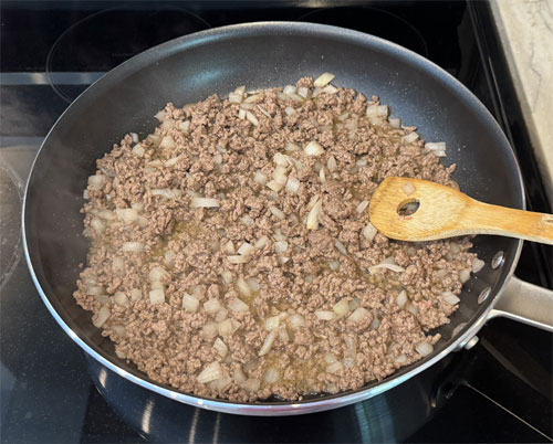 Heat a large skillet over medium heat. Once it's hot, lightly coat it with olive oil spray. Then, add the beef and chopped onion. Break apart and turn the meat and onions until it's no longer pink.