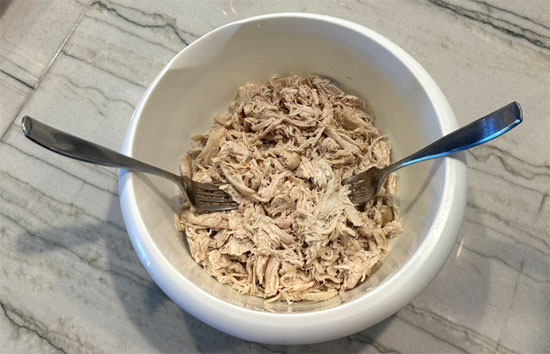 Shred the chicken. You can do it with two forks, tearing it apart, but using a hand or stand mixer is really easy. You put the chicken in the bowl and use the paddle attachment. Turn it on medium for about 30 seconds, and it'll completely shred it. A regular-sized mixer can handle up to 5 chicken breasts, while the large ones can handle up to 10. 