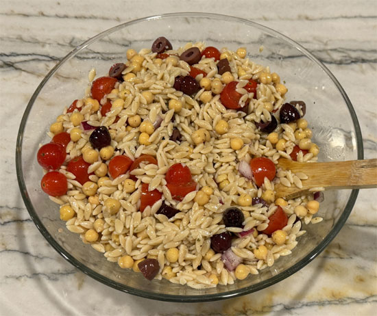 Pour half the dressing over the hot orzo. Add chickpeas, tomatoes, and olives. Toss well.