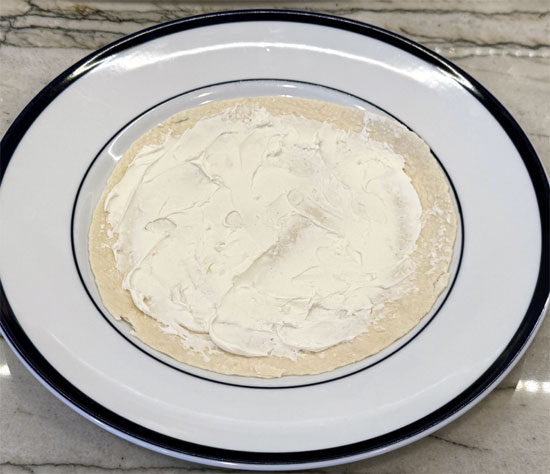 Lay the tortilla wrap flat and spread the reduced-fat cream cheese evenly on top.